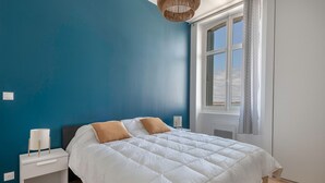 A bedroom with a large bed, white bedding, a nightstand with a lamp, and a window with curtains. - Seaview in the heart of le Croisic (Le Croisic)