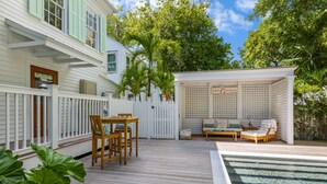 A wooden deck with a pool, outdoor seating, and a white fence.