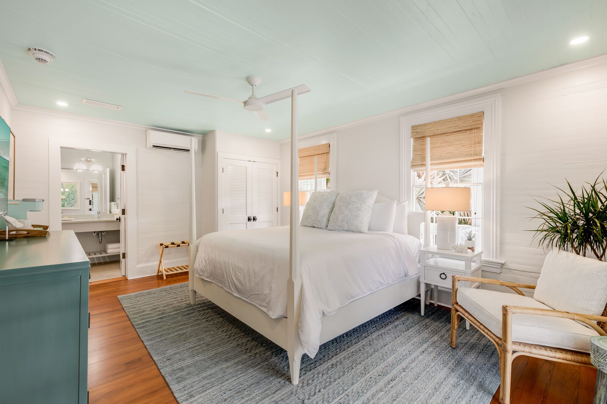 Une chambre à coucher avec un lit à baldaquin, une table de chevet avec une lampe, une chaise et une grande fenêtre avec des stores.
