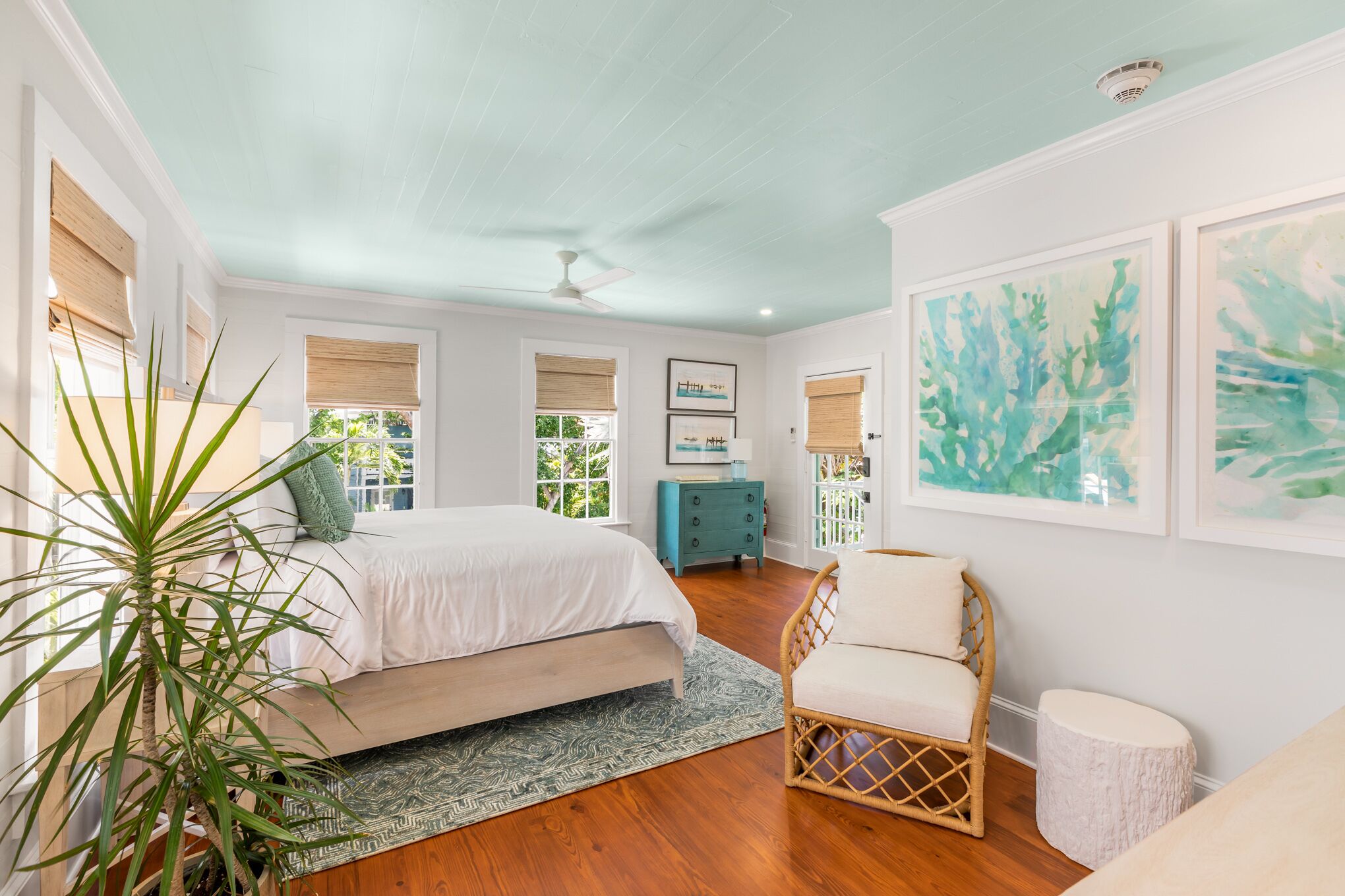 A bedroom with a bed, a chair, a small table, and a potted plant.
