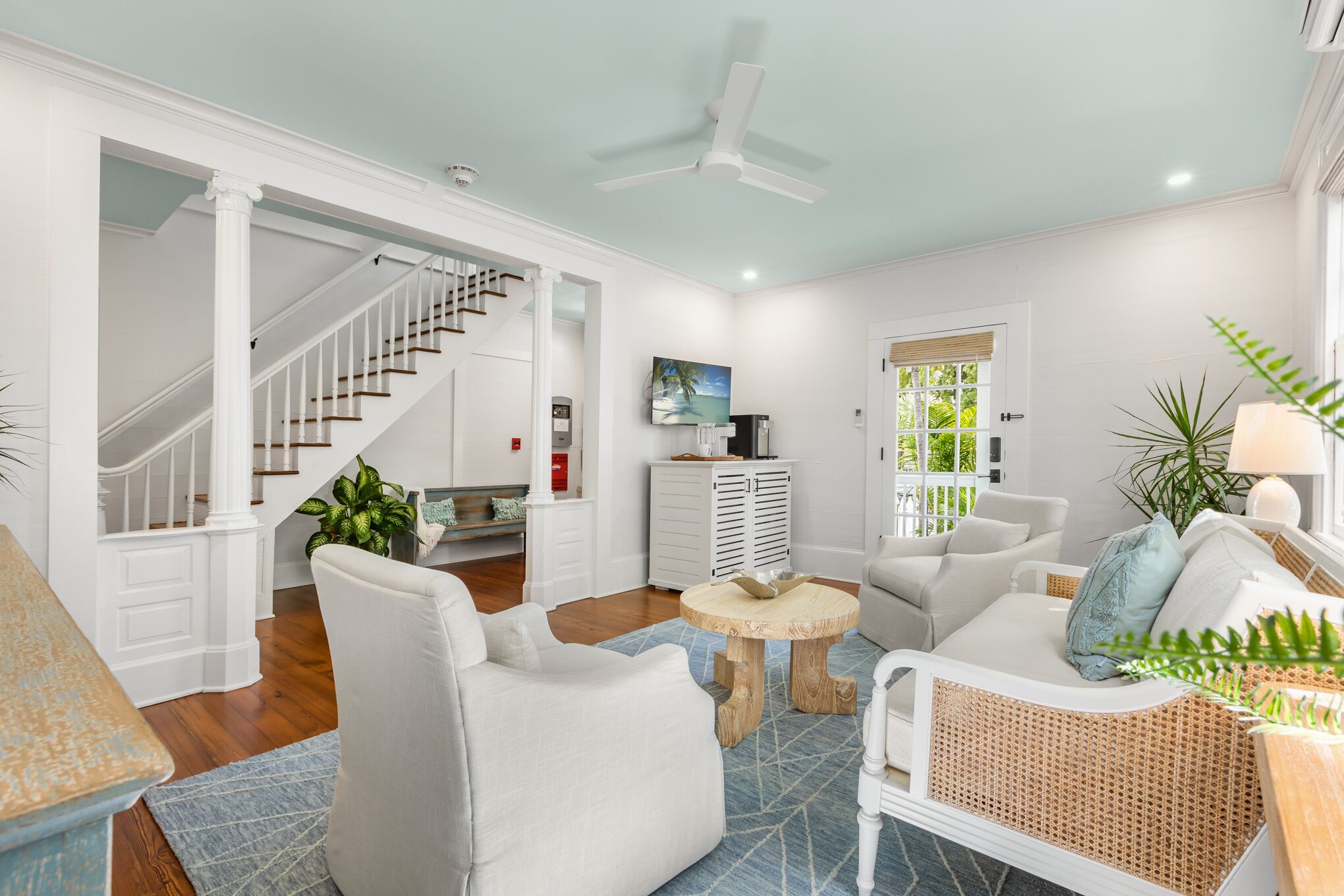 A spacious living room with a staircase, white furniture, and a ceiling fan.