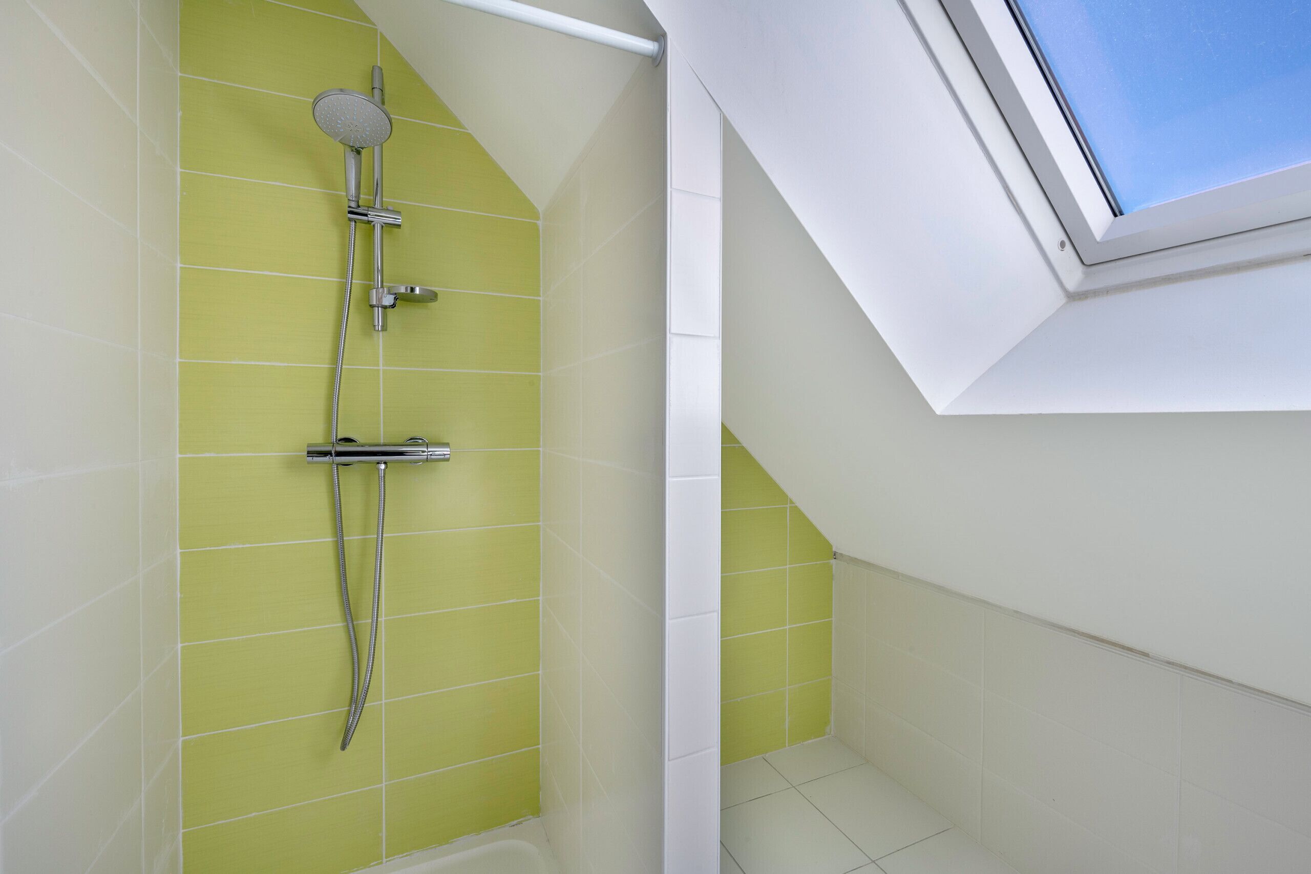 Une salle de bain avec une douche, un puits de lumière et un carrelage au sol.