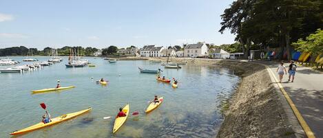 A calm harbor with several kayaks and boats, a stone wall, and a clear sky.