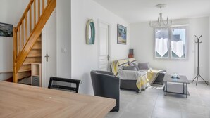 Ein modernes Wohnzimmer mit einer Holztreppe, einer Couch, einem Esstisch und einer Pendelleuchte.