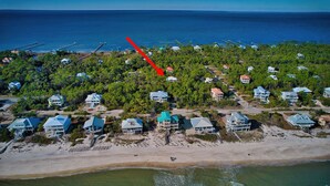 An aerial view of a coastal residential area with houses, a beach, and a pier.