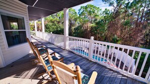 A wooden deck with a pool, white railings, and a view of trees.