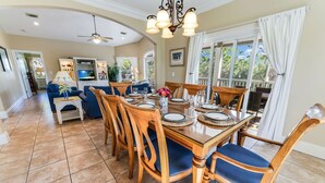 A dining area with a wooden table set for six, surrounded by six wooden chairs with blue cushions.