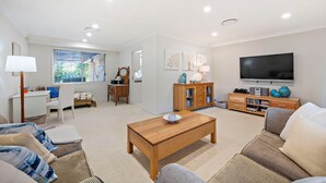 Ein modernes Wohnzimmer mit Couch, Fernseher, Bücherregal und einem Holztisch.