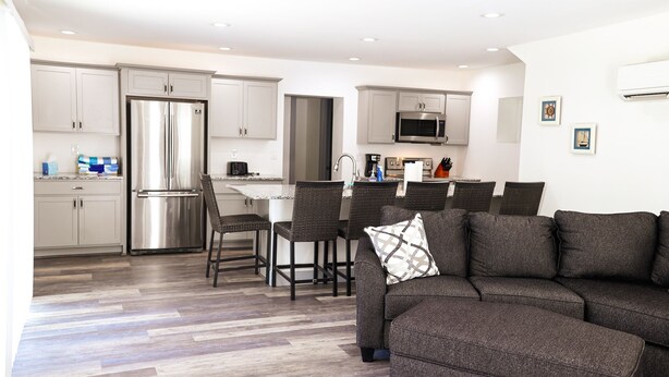 Een moderne keuken met roestvrijstalen apparatuur, een eethoek met rieten stoelen en een grijze bank in een woonkamer.
