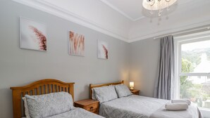 A hotel room with two beds, a nightstand with a lamp, and a window with curtains. - White Roses (Ross-on-Wye)