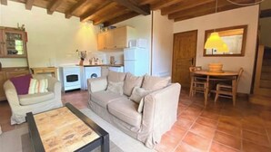 Een gezellige woonkamer met een bank, een salontafel en een eethoek met een tafel en stoelen. Er is een keuken met een koelkast en een wasmachine.