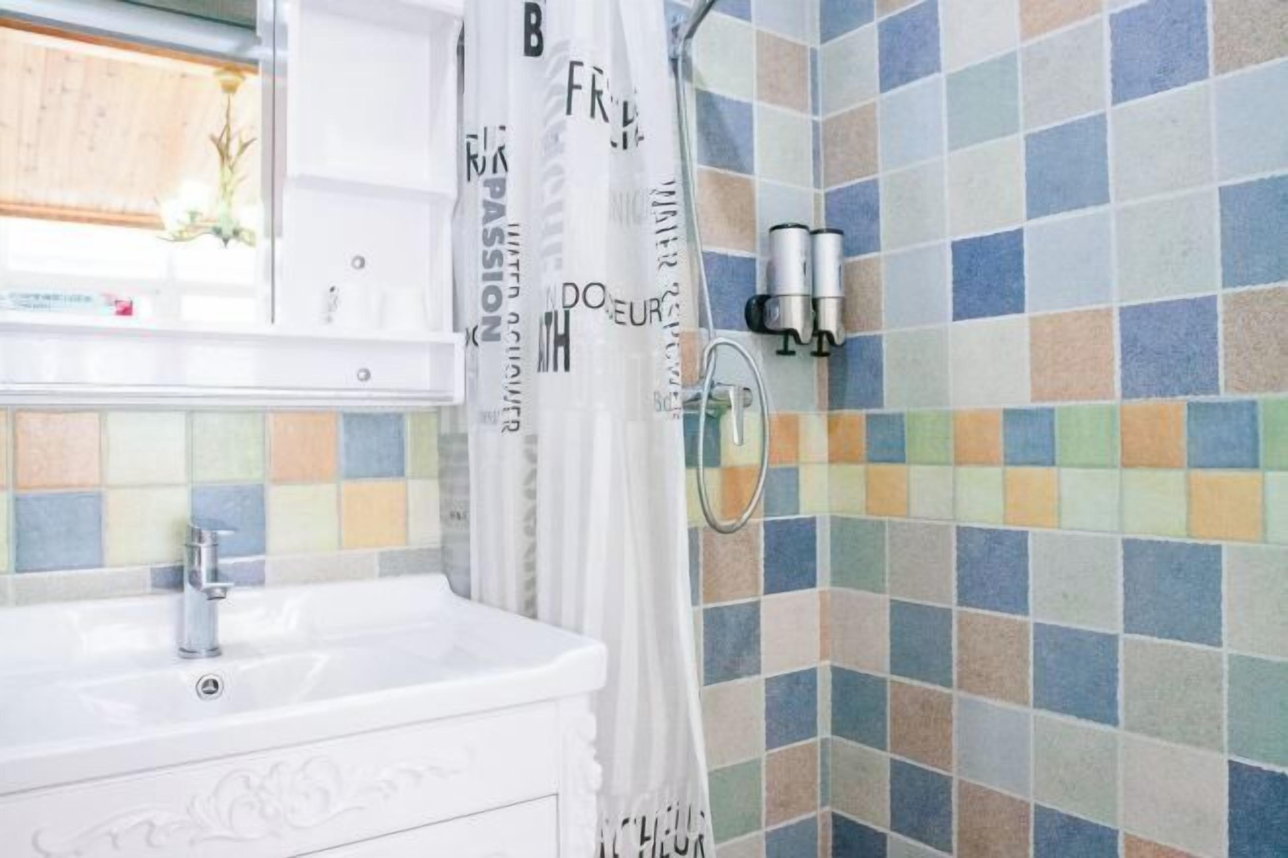 A bathroom with a white sink, a shower curtain with text, and a tiled wall.