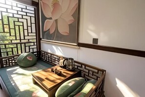 Ein traditioneller japanischer Raum mit Tatami-Bodenbelag, einem niedrigen Holztisch, einer grünen gepolsterten Sitzbank und einem großen Blumenbild an der Wand.