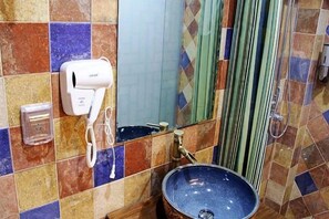 Een badkamer met een betegelde muur, een wastafel met een blauwe kom, een haardroger en een douchegordijn.