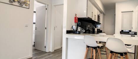 A modern kitchen with white cabinets, a black range hood, and a bar area with stools.