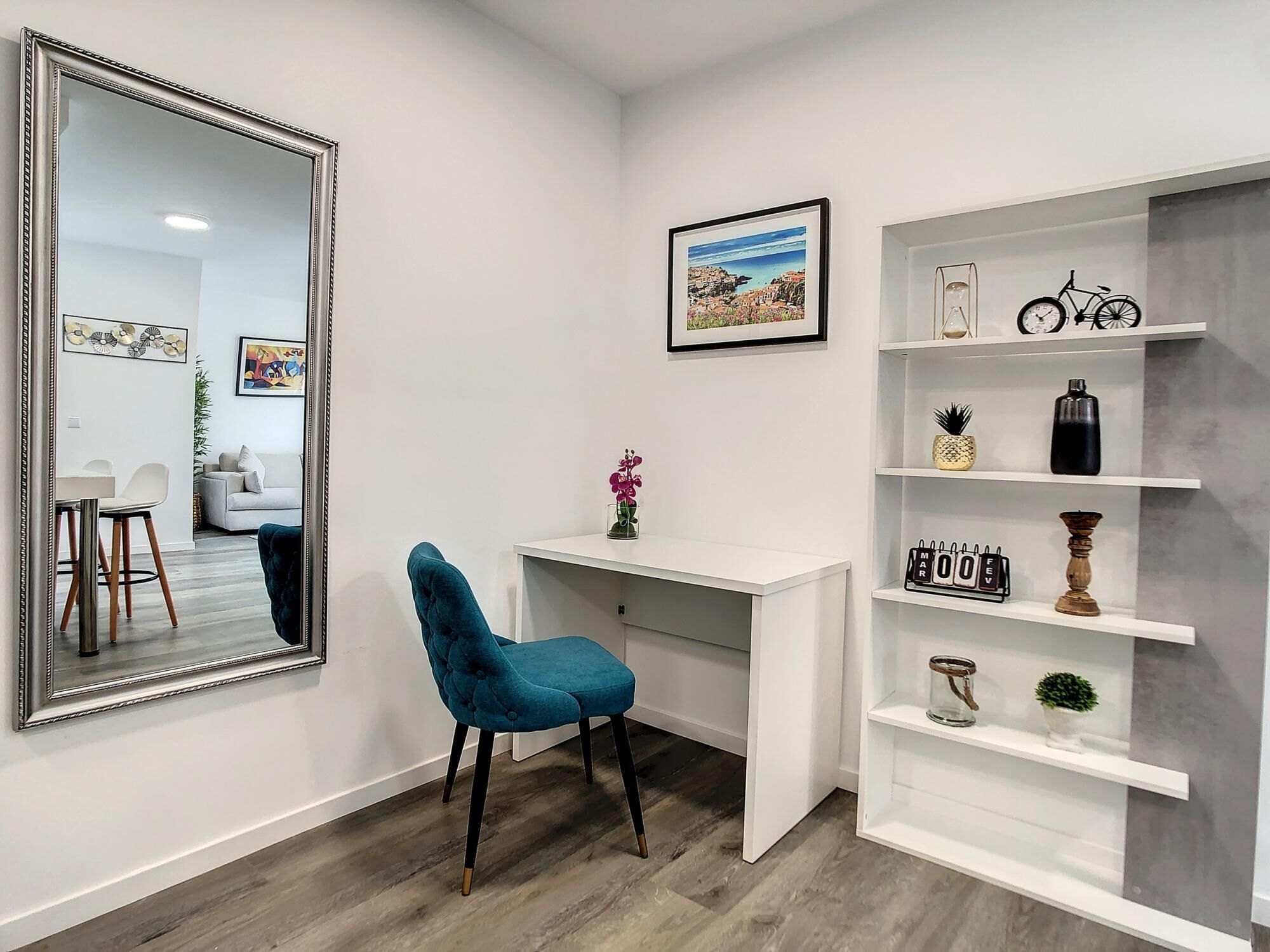 A modern room with a large mirror, a desk with a chair, a bookshelf, and a framed picture on the wall.