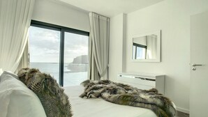 Quarto moderno com uma janela grande, uma cama com cobertor macio e uma mesa de cabeceira branca.
