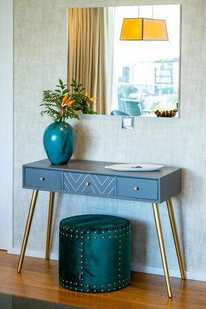Un mueble de baño moderno con un jarrón turquesa, un espejo y un taburete.