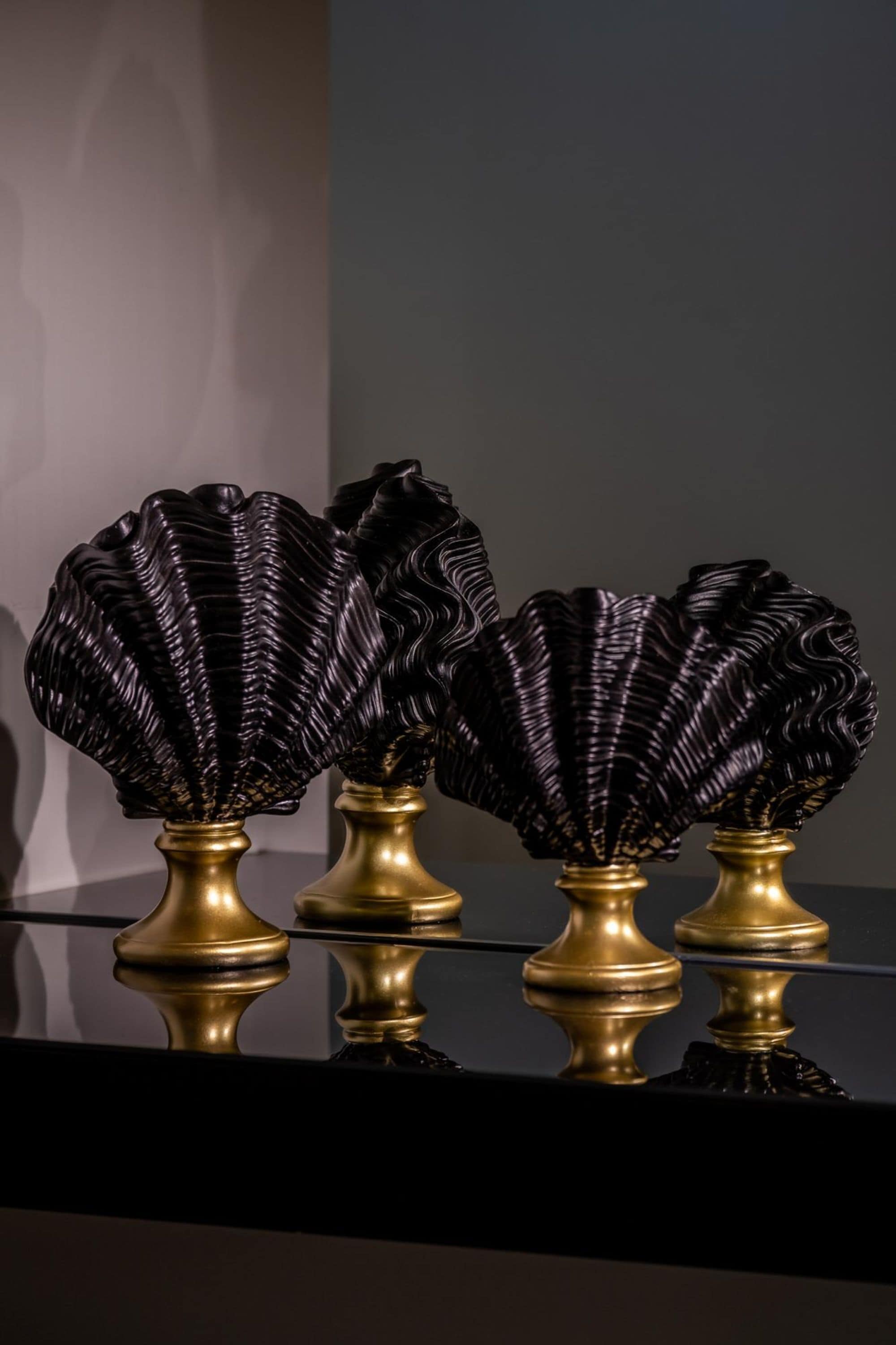 Drie zwarte en gouden decoratieve vazen op een reflecterend oppervlak.