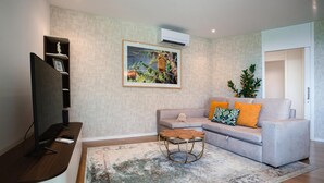 Ein Wohnzimmer mit einer Couch, einem Couchtisch, einem Fernseher und einem gerahmten Bild an der Wand.