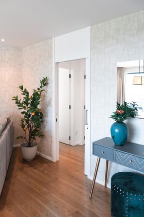 A modern room with a wooden floor, a grey sofa, a blue desk with a decorative vase, and a potted plant.