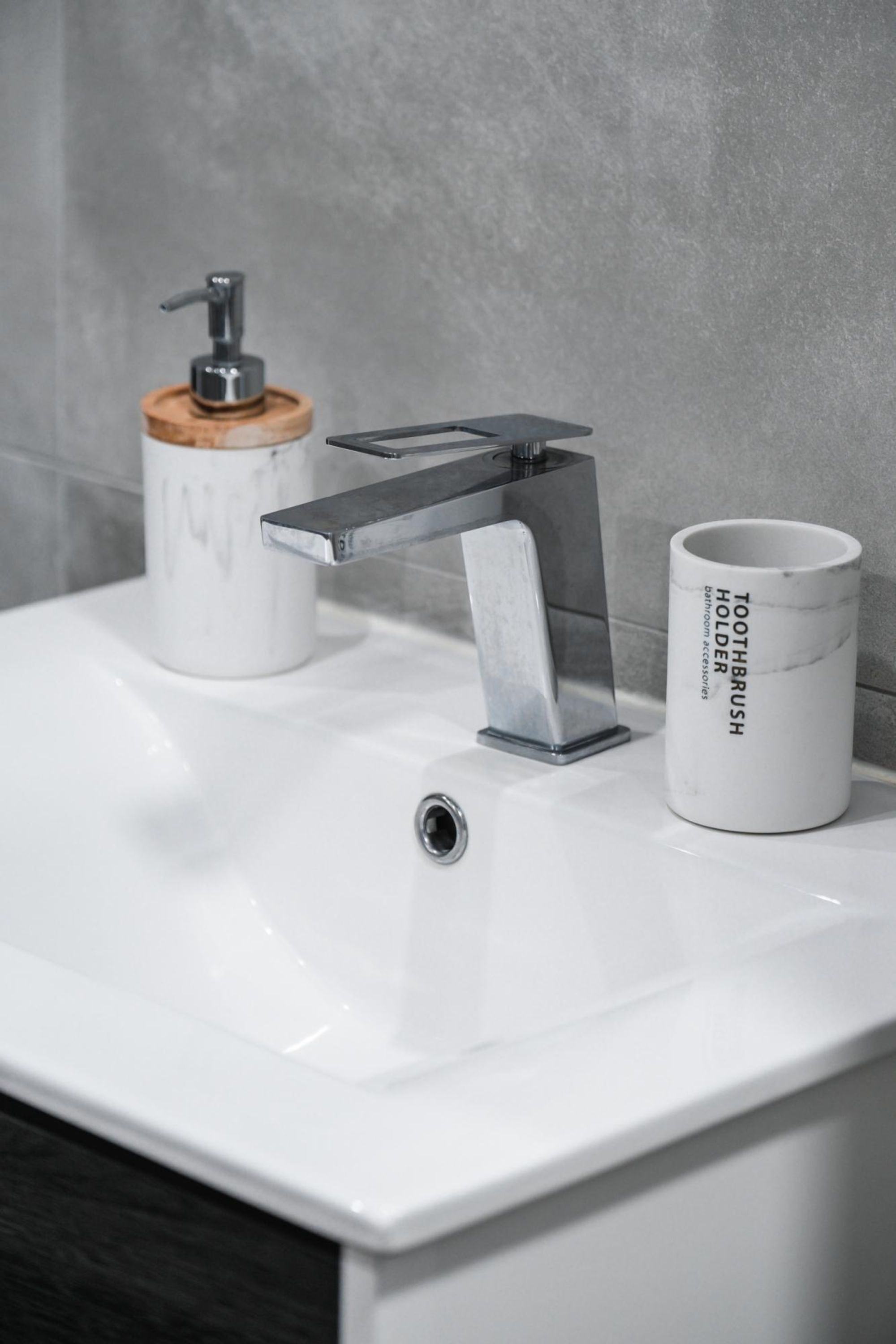 A bathroom sink with a modern faucet, a toothbrush holder, and a cup labeled "TOOTHBRUSH HOLDER".