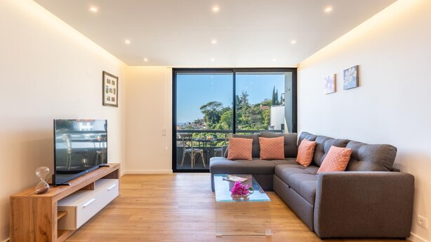 A modern living room with a sofa, TV, and wooden floor. - Magn lia Apartment by Atlantic Holiday (Funchal)
