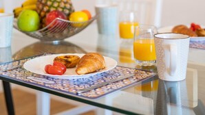 A breakfast table with a plate of croissants, tomatoes, and a pineapple. There are also glasses of orange juice and a bowl of fruit. - Magn lia Apartment by Atlantic Holiday (Funchal)