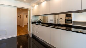 A modern kitchen with white cabinets, black countertops, and stainless steel appliances. - Magn lia Apartment by Atlantic Holiday (Funchal)