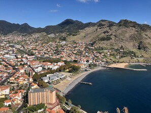 A coastal town with a mix of residential and commercial buildings, a beach, and mountains in the background.