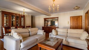 Una sala de estar con dos sofás beige, una mesa de centro de cristal, armarios de madera y una araña.