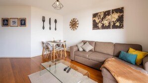 A living room with a sofa, a glass coffee table, a dining table with chairs, a wall clock, and a world map artwork. - Sea View by Atlantic Holiday (Santa Cruz)