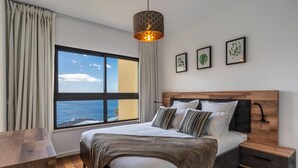 A modern bedroom with a large window, a wooden headboard, a bedside table, and a hanging light fixture. - Centromar Bella Vista by Atlantic Holiday (Funchal)