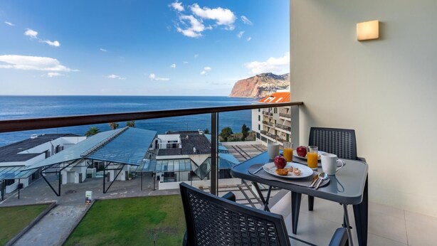 A balcony with a table set for breakfast, overlooking a coastal view with buildings and a cliff. - Centromar Bella Vista by Atlantic Holiday (Funchal)