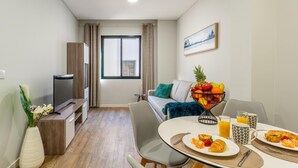 Un espace de vie compact comprenant un coin repas, un canapé, un téléviseur et une fenêtre avec des rideaux.