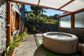 A hot tub in a courtyard with stone walls, potted plants, and a view of a garden. - Stone House Vista II by Atlantic Holiday (São Vicente)