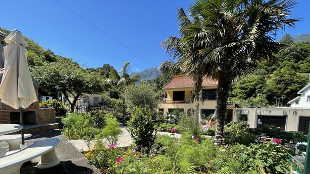 A garden with a stone bench, a hammock, and a house with a red roof. - Stone House Vista by Atlantic Holiday (São Vicente)
