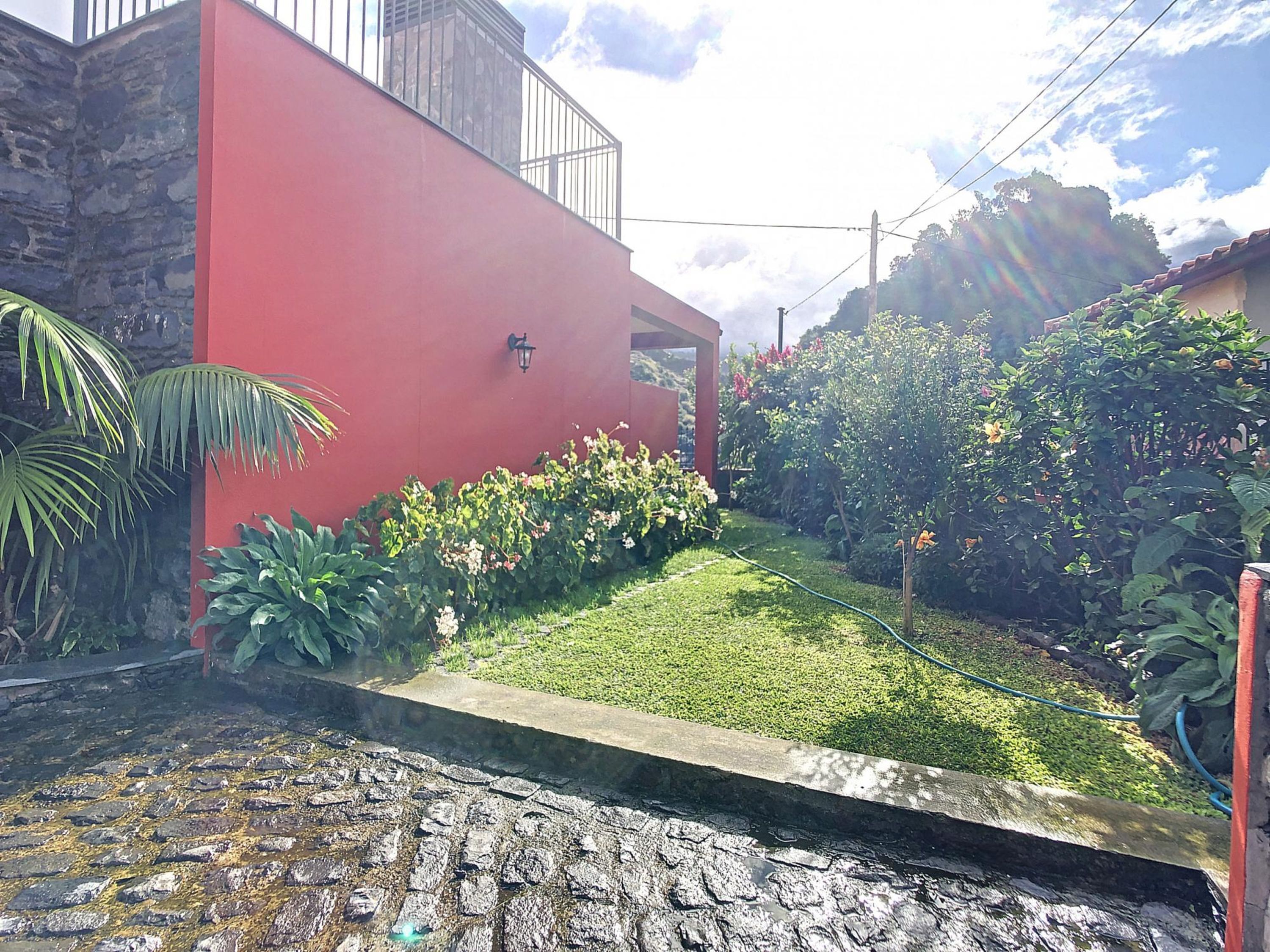 A red building with a stone wall, a grassy area with plants, and a cobblestone path.