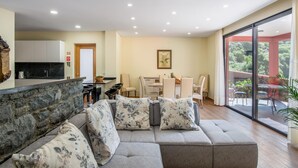 A modern living room with a grey sofa, a kitchen area, and a dining space. - Villa Teresa 1 by Atlantic Holiday (São Vicente)