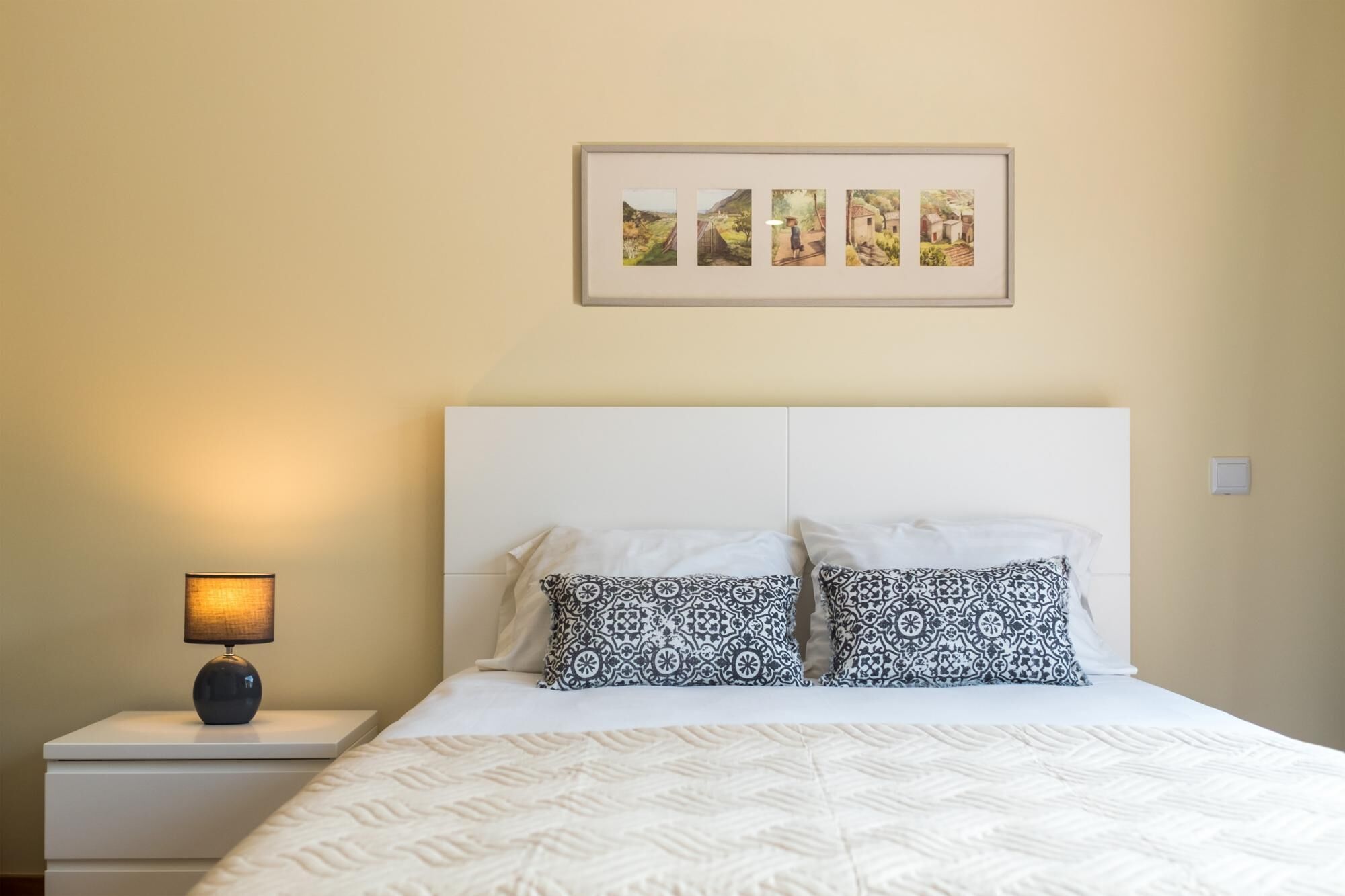 A neatly made bed with patterned pillows, a bedside lamp, and a framed picture above it.