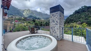 Jacuzzi en un balcón con vista a la montaña, un pilar de piedra y barandilla.