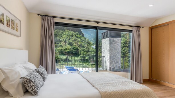 Un dormitorio con una cama grande, vistas a un balcón con mobiliario exterior y un pilar de piedra.