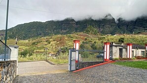 Un camino empedrado que lleva a una entrada con puerta de hierro forjado, con montañas al fondo.
