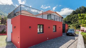 Un edificio rojo con un balcón de vidrio, un camino de adoquines y un coche estacionado.