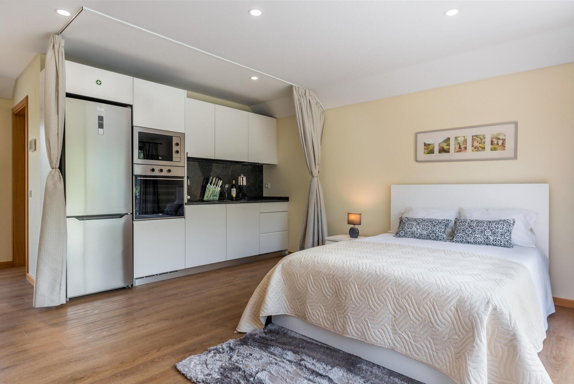 A compact bedroom with a bed, a nightstand, and a small table with a lamp.