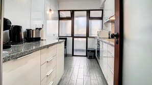 Una cocina moderna con armarios blancos, encimeras de granito y un amplio ventanal con paneles de vidrio esmerilado.
