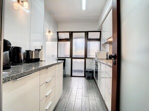 Una cocina moderna con armarios blancos, encimeras de granito y un amplio ventanal con paneles de vidrio esmerilado.