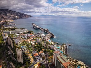 A coastal cityscape with a cruise ship docked at a pier, surrounded by residential buildings and a large hotel with a pool.