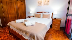 Habitación de hotel impecable con una cama grande, un armario de madera, dos mesitas de noche con lámparas y una ventana con cortina roja.