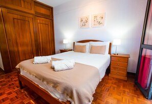 Habitación de hotel impecable con una cama grande, un armario de madera, dos mesitas de noche con lámparas y una ventana con cortina roja.